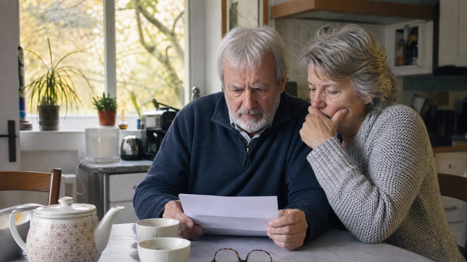 Un couple de retraités lit un courrier de sa caisse de retraite complémentaire à la table de sa cuisine