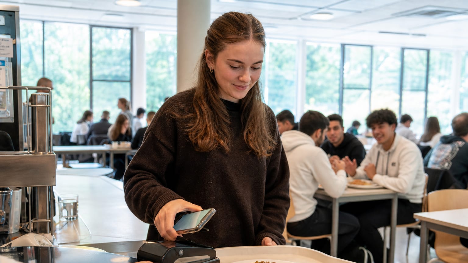 Une étudiante paie son plateau-repas au restaurant universitaire avec son téléphone