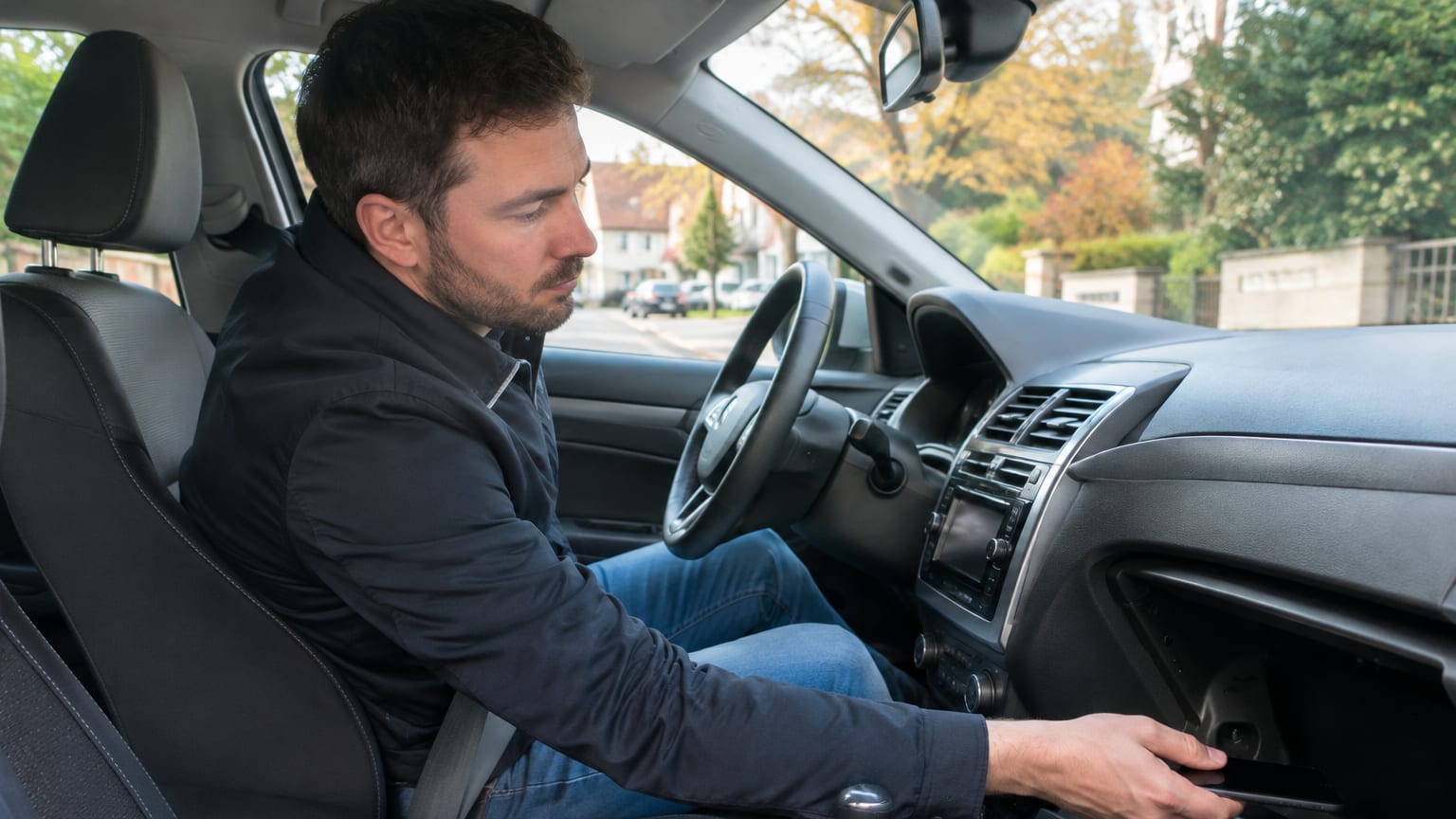 Un conducteur range son téléphone dans la boîte à gants avant de démarrer sa voiture